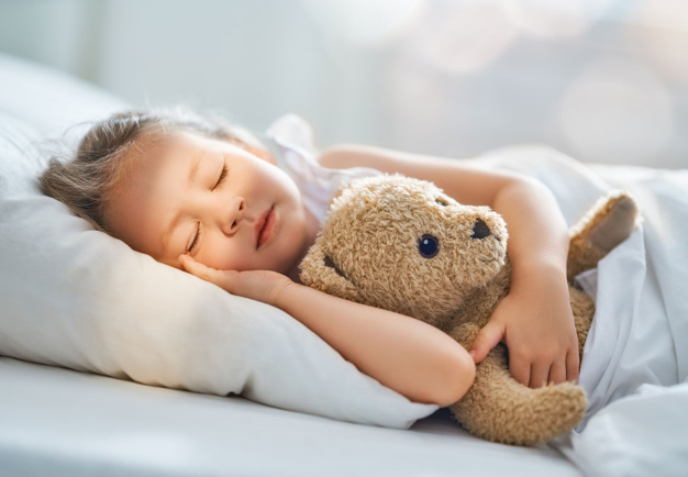 girl sleeping in bed with teddy bear